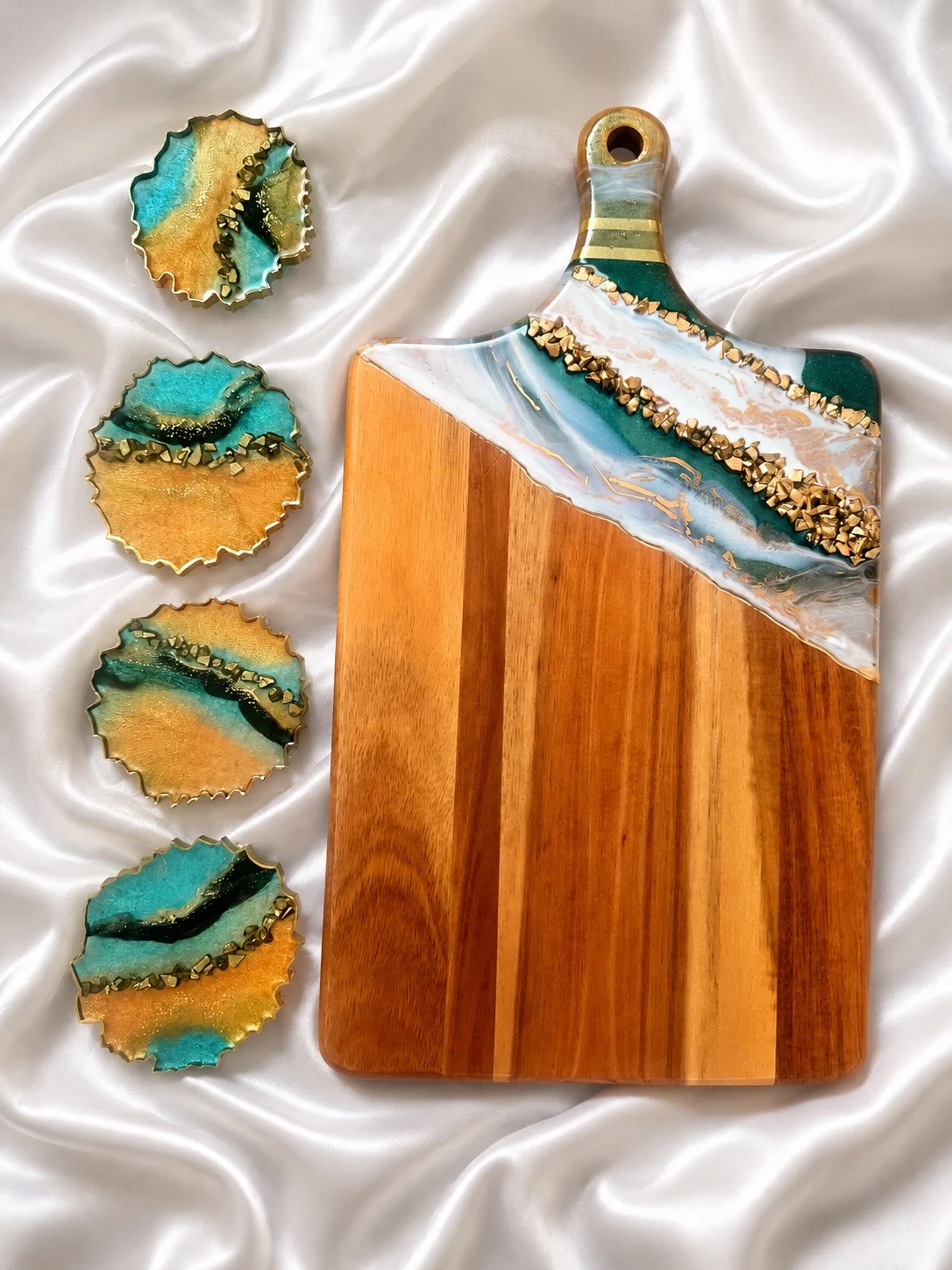 Set artesanal de tabla para servir y cuatro posavasos a juego, decorados con resina epoxi en tonos turquesa, verde y dorado con detalles texturizados en color oro.